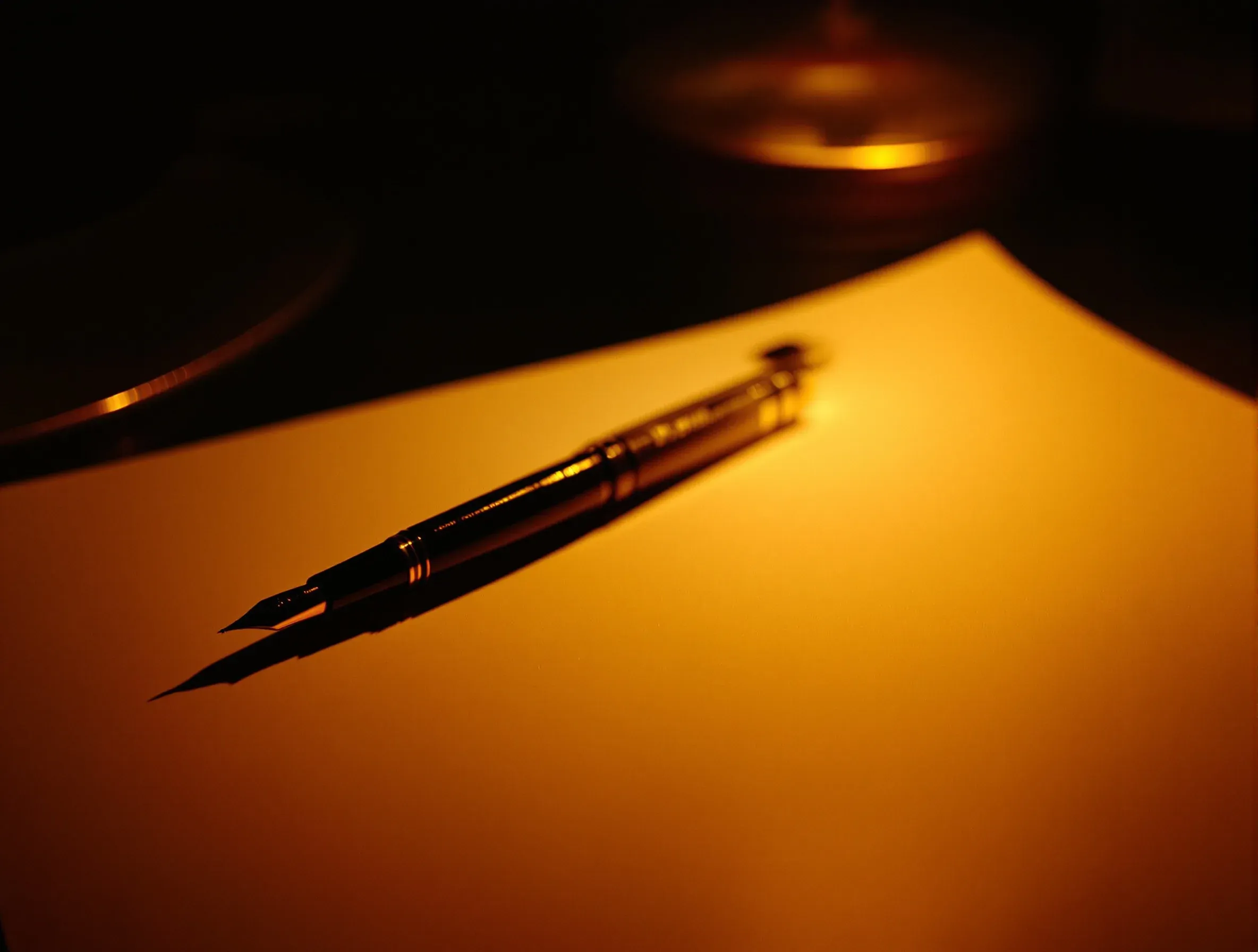 A fountain pen lying across a sheet of blank paper on a dark desk