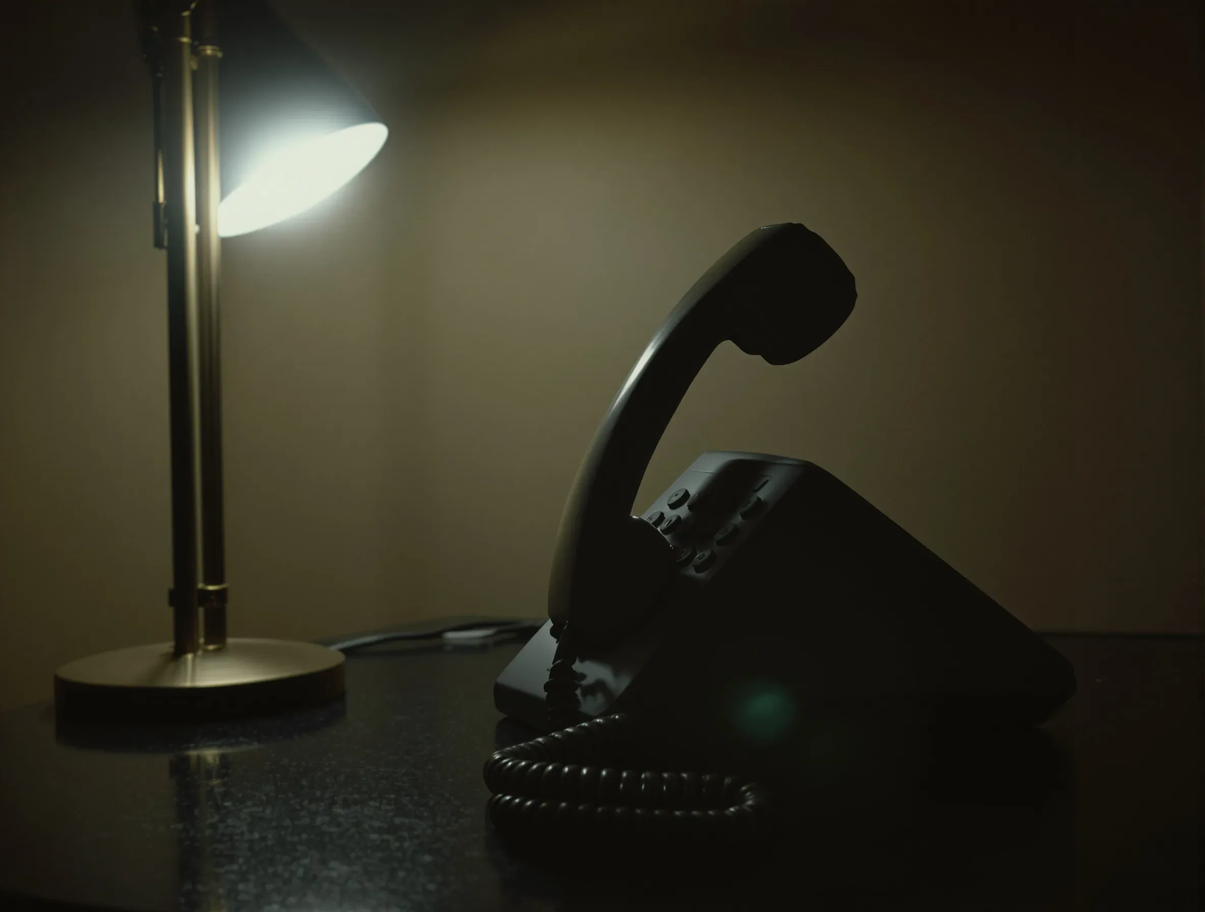 A corded telephone handset lifted off its cradle and resting on a dark desk