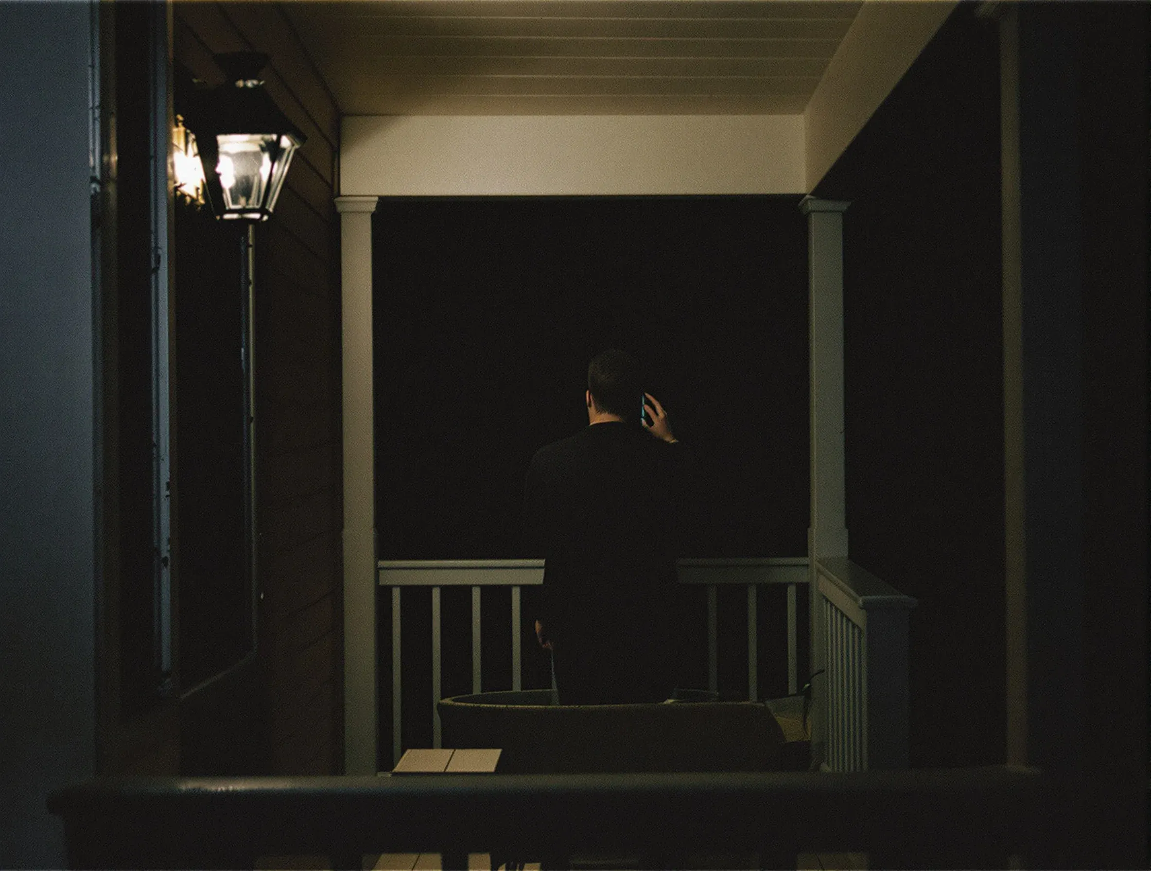 A person on a porch at night, seen from behind, holding a phone to their ear